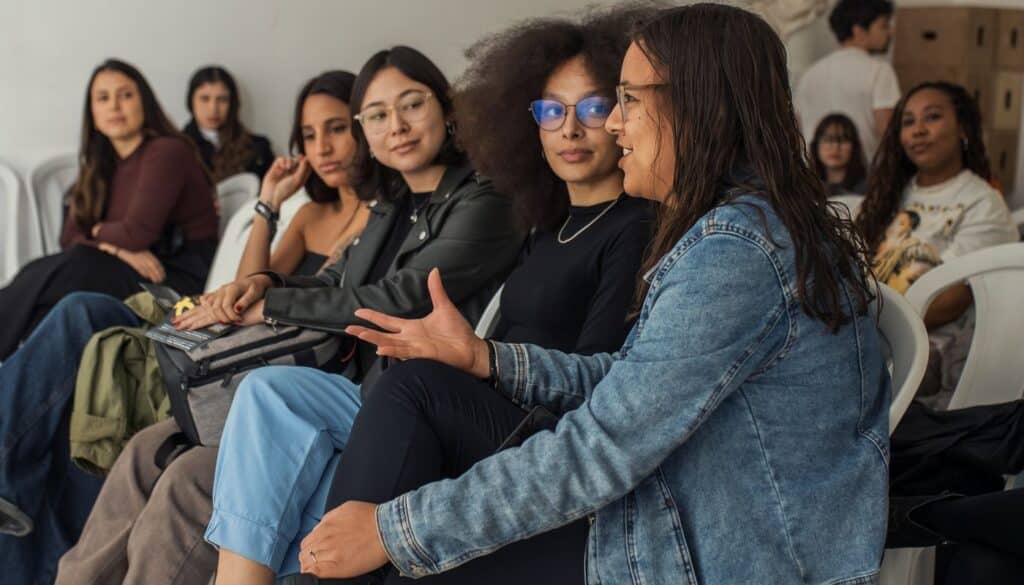 Diverse group of adult learners seated together in a bright indoor workshop room listening during an in person training session