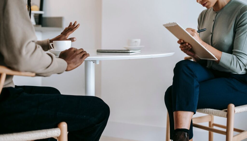 A lifestyle coach listening and writing notes while a client talks through their daily routine