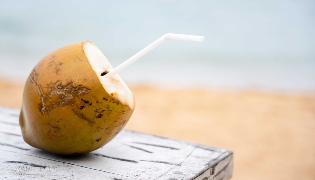 A fresh green coconut opened with a drinking straw on a wooden table, one of the sweet cooling foods that settles excess pitta