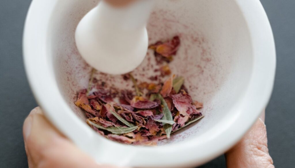 Close up of hands grinding dried herbs and petals with a stone mortar and pestle while learning Ayurvedic preparation by doing