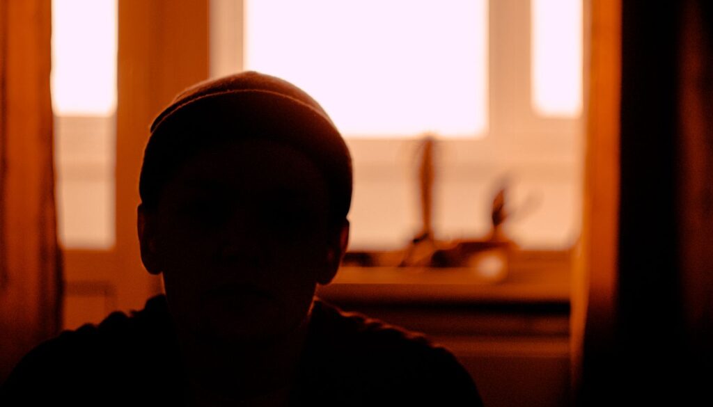 A person sitting still in silhouette against soft window light in a dim room, settled into early morning practice