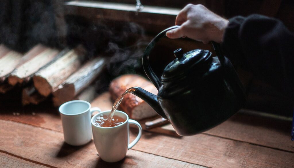 Warm tea being poured into a white ceramic mug in soft early morning light