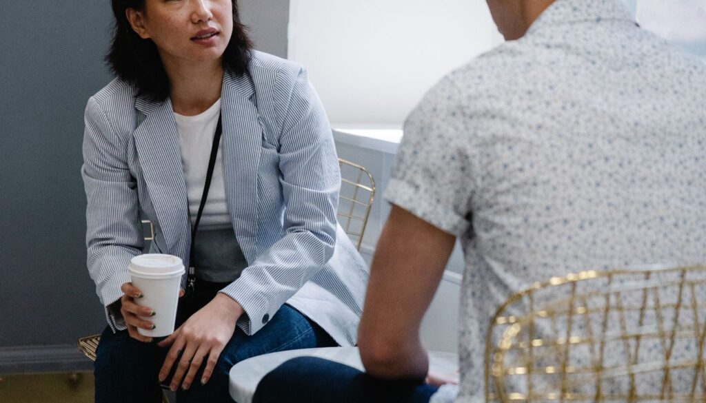 Two people sitting and talking over coffee in a relaxed cafe setting during an informal lifestyle coaching conversation