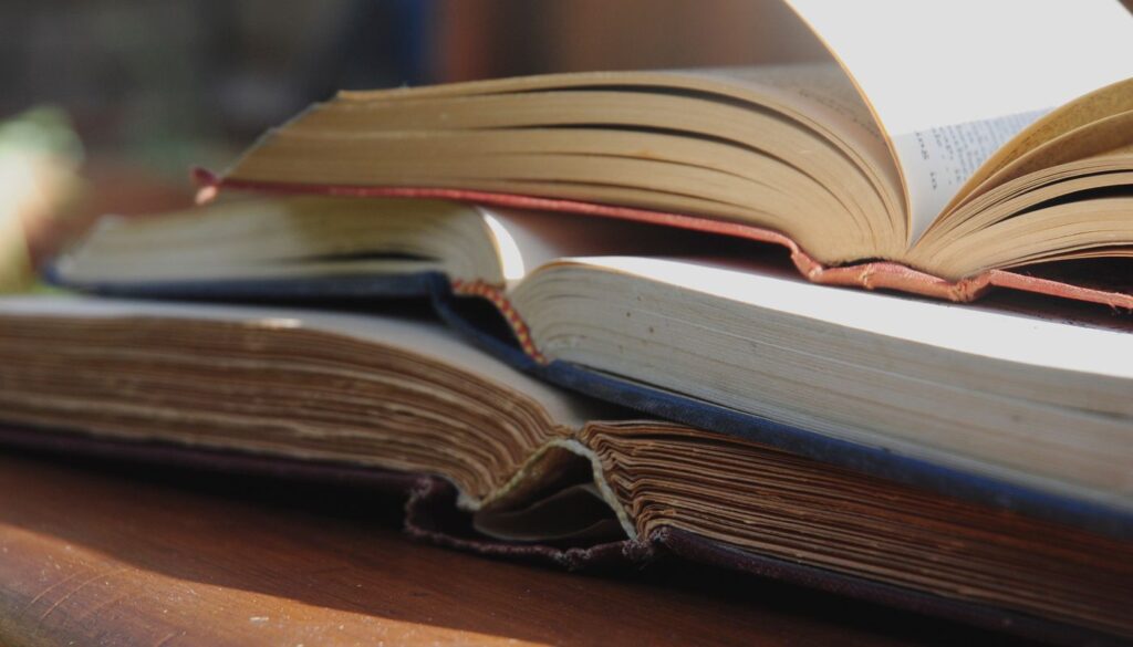 Stack of opened books resting on a sunlit wooden table, ready for a session of Ayurveda reading