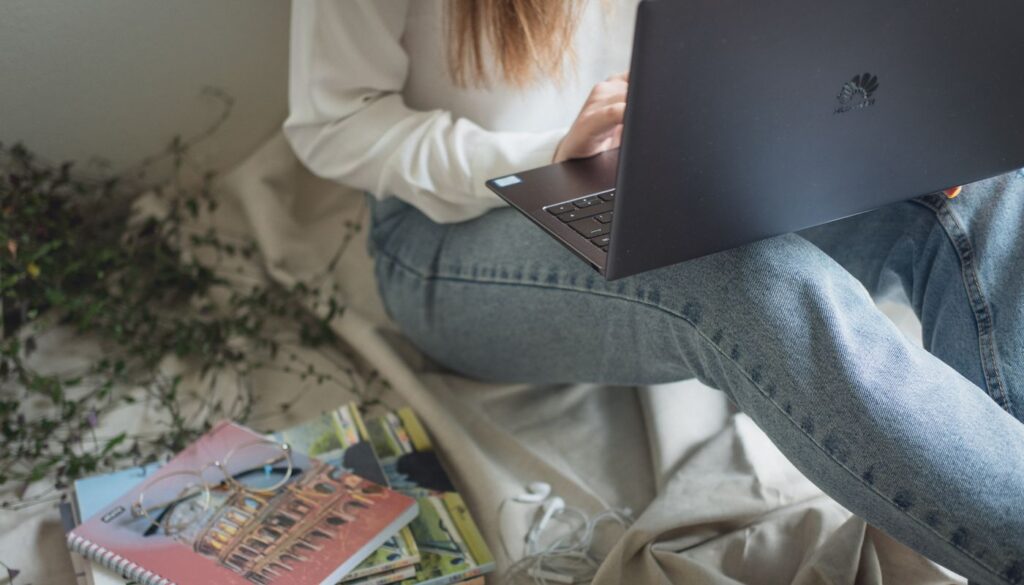 Woman studying at a desk with a laptop and open textbooks while working through foundational Ayurveda coursework